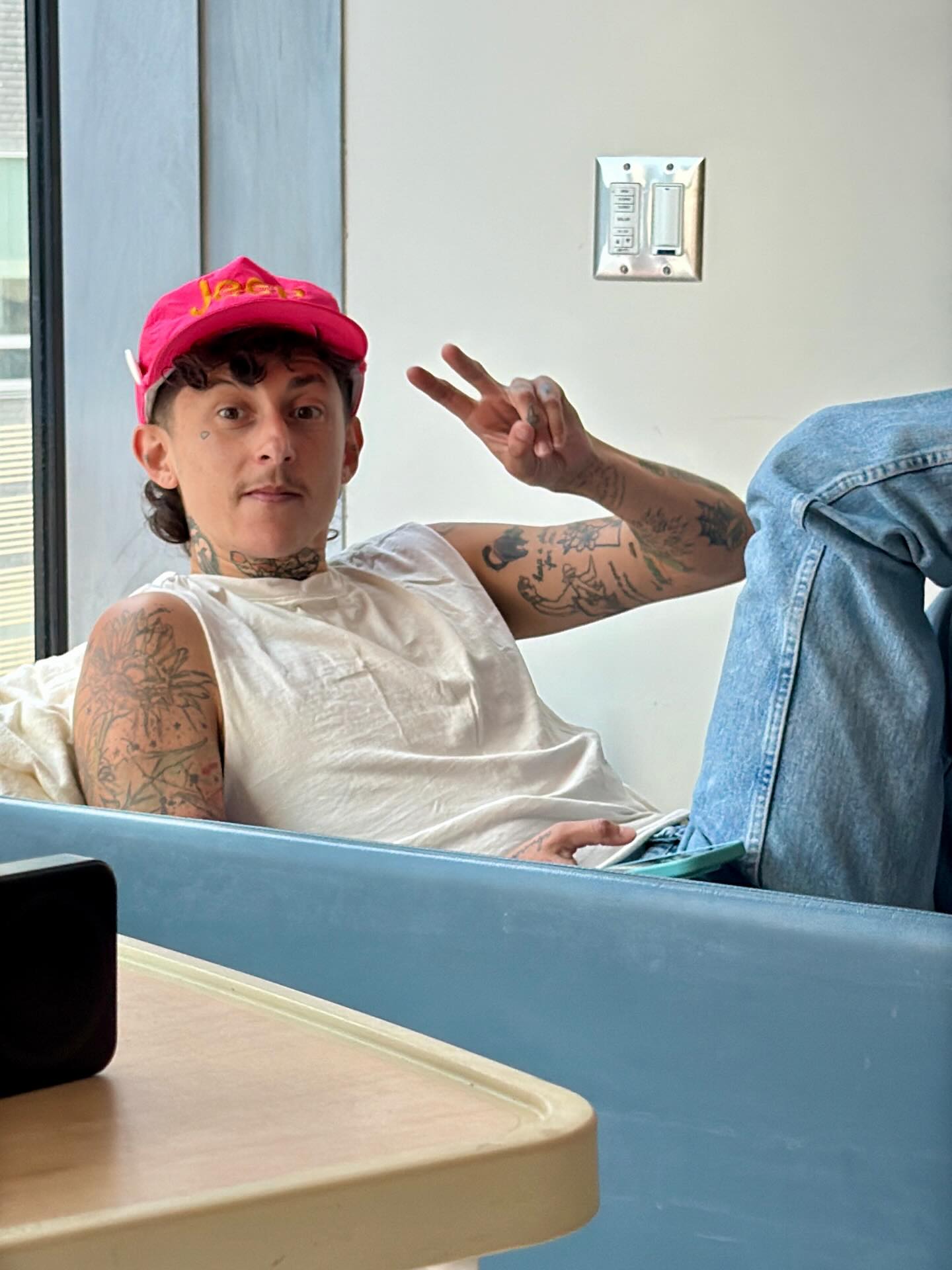 A visitor in a red cap sitting beside the hospital bed.