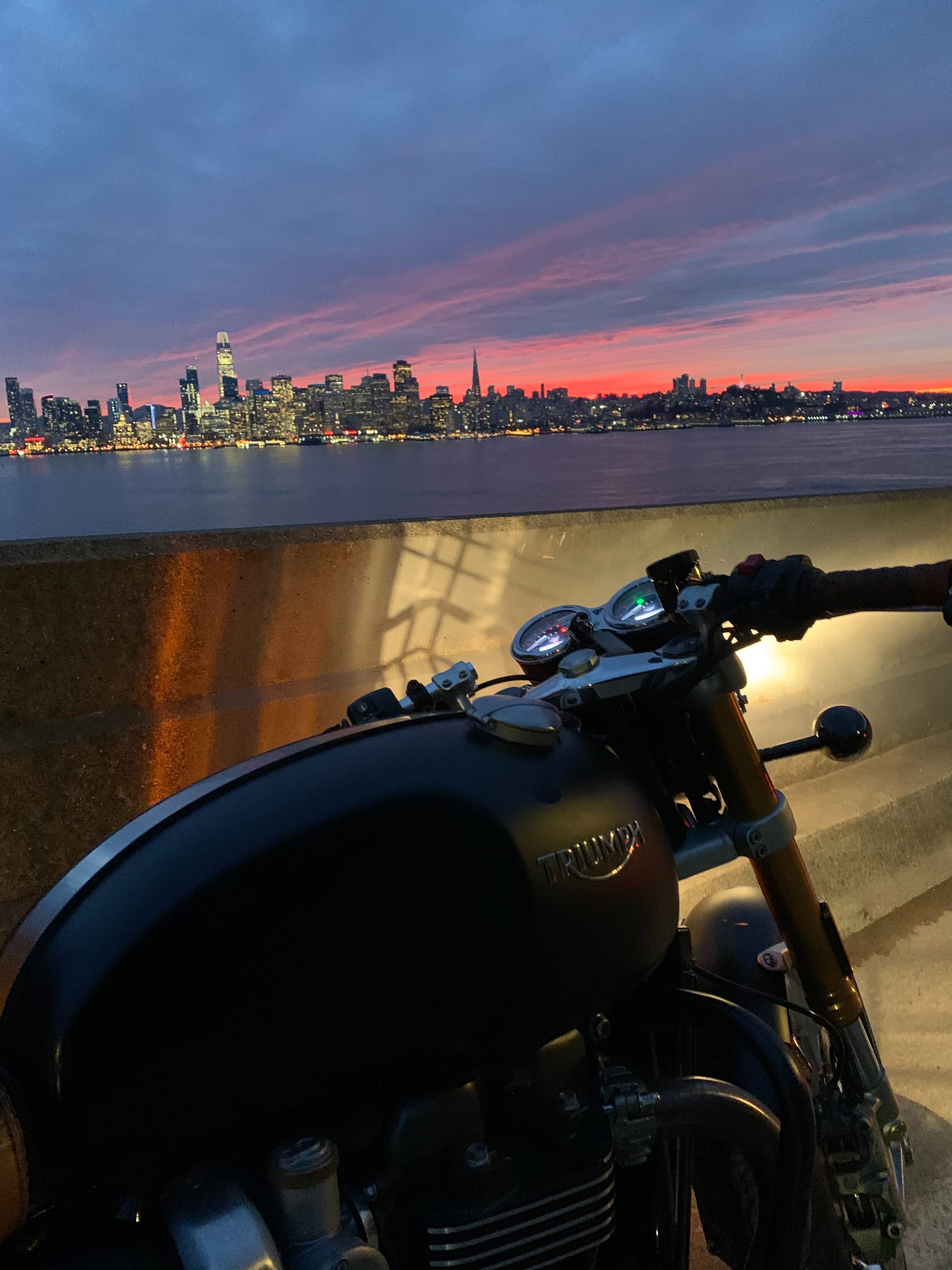 The Triumph beside the waterfront under a pink and purple sunset.
