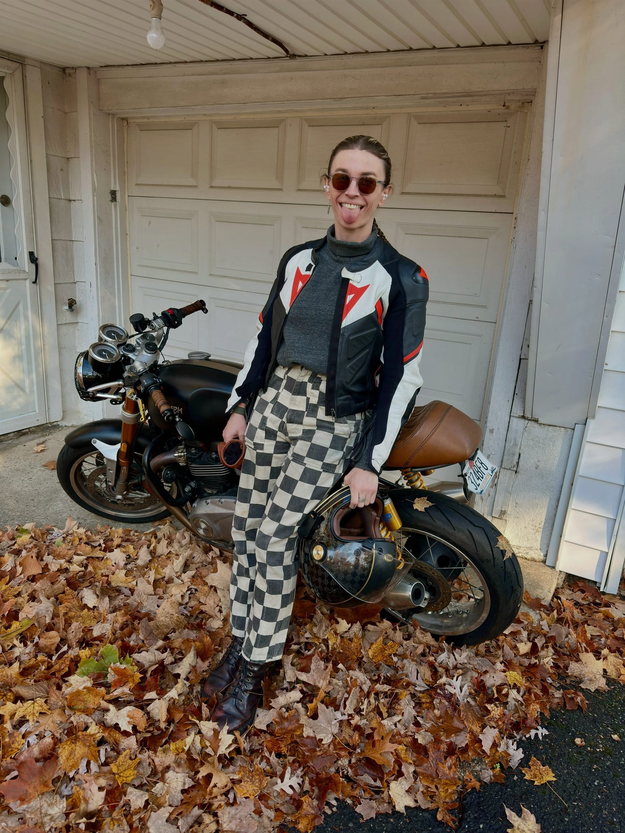 Grace in a motorcycle jacket and checked trousers beside her Triumph.